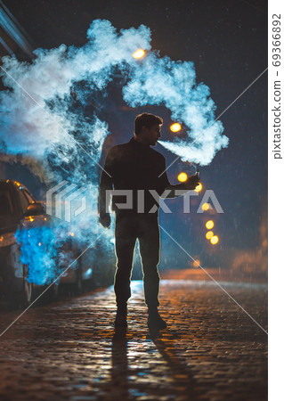 The man smoke electrical cigarette in the street. Evening night time 69366892