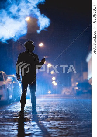 The man smoke electrical cigarette on the street. Evening night time 69366917