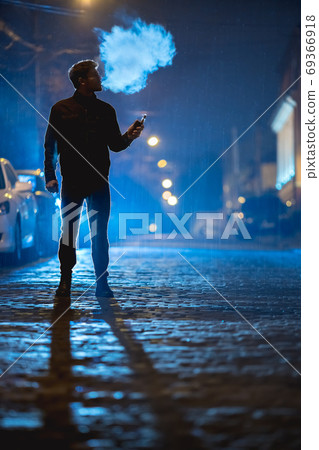 The man smoke electrical cigarette on the street. Evening night time 69366918
