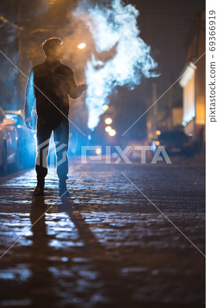 The man smoke electronic cigarette on the street. Evening night time 69366919