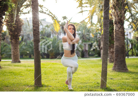 Woman in white sports outfit performing Yoga Eagle pose outdoor, in park meadow. 69367000