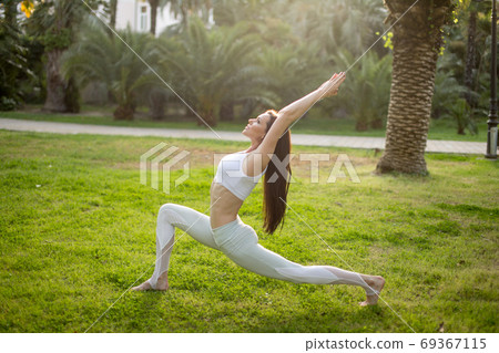Woman practicing Warrior yoga pose outdoors over green nature background. 69367115