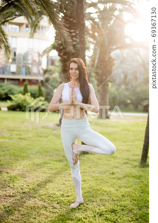 Attractive woman doing yoga tree pose, balancing on one leg, with raised hands. Attractive woman doing yoga tree pose, balancing on one leg, with raised hands. 69367130