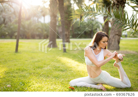 Woman practicing yoga in park, sitting in One Legged King Pigeon exercise Woman practicing yoga in park, sitting in One Legged King Pigeon exercise 69367626