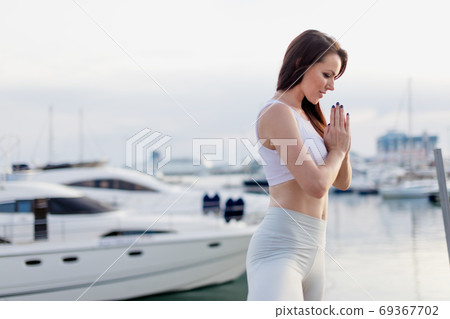 Woman doing yoga at pier. Woman relaxing at the seaside dock in tree pose. 69367702
