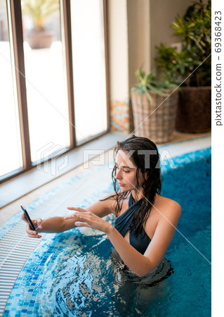 Young happy girl taking a selfie in indoor pool at wellness center Young happy girl taking a selfie in indoor pool at wellness center 69368423