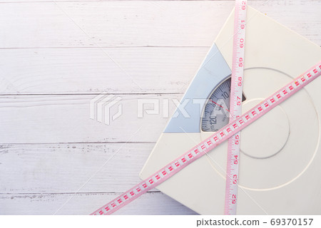 a tape measure and Bathroom scale on wooden floor. 69370157