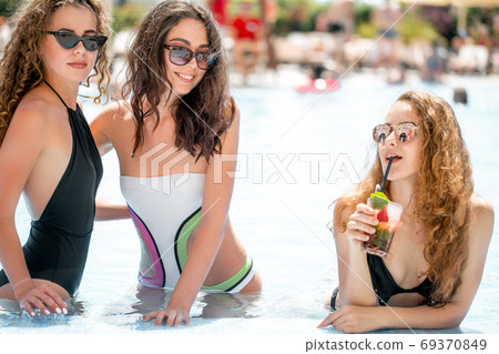 Cute girlfriends with cocktail glass chilling in the tropical sun in swimming pool. Vacation concept 69370849