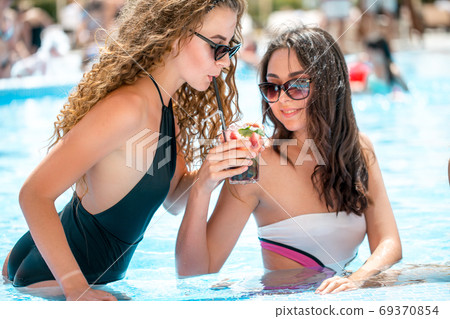 Cute girlfriends with cocktail glass chilling in the tropical sun in swimming pool. Vacation concept 69370854