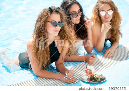 Cute girlfriends with cocktail glass chilling in the tropical sun in swimming pool. Vacation concept 69370855