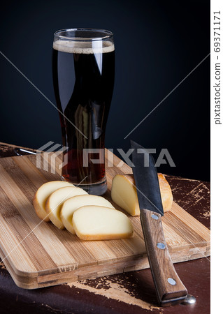 Glass with dark beer with smoked cheese on cutting board. Glass with dark beer with smoked cheese on cutting board. 69371171