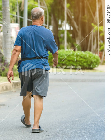Back view portrait of a Asian elderly man in fitness wear walking and jogging for good health in public park. Senior jogger in nature.  Older Man enjoying Peaceful nature. Healthcare concept. 69371487