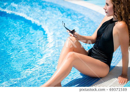 Young woman sitting on the ledge of the pool. 69371589