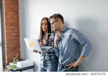happy mix-race couple holding laptop computer while standing and celebrating isolated over gray wall background 69374170