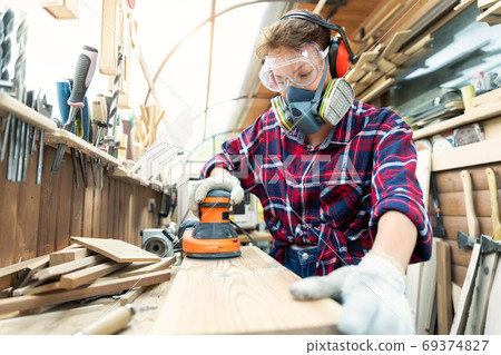Young adult caucasian mid aged professional female carpenter grinding raw wood with orbital sander Young adult caucasian mid aged professional female carpenter grinding raw wood with orbital sander 69374827