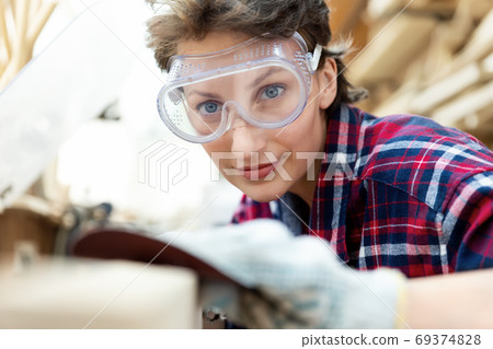 Young adult caucasian mid aged professional female carpenter grinding raw wood with orbital sander Young adult caucasian mid aged professional female carpenter grinding raw wood with orbital sander 69374828