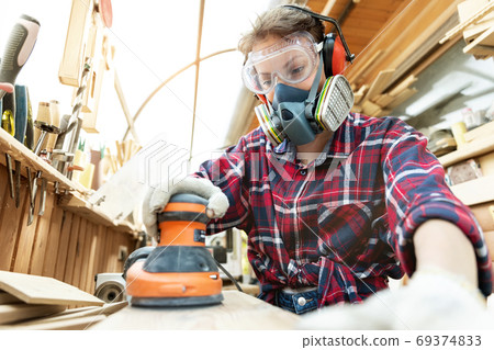 Young adult caucasian mid aged professional female carpenter grinding raw wood with orbital sander Young adult caucasian mid aged professional female carpenter grinding raw wood with orbital sander 69374833