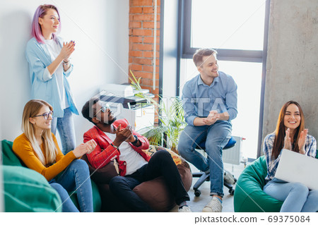 Young handsome man in glasses gesturing and discussing something with his coworkers while sitting at the office table Young handsome man in glasses gesturing and discussing something with his coworkers while sitting at the office table 69375084