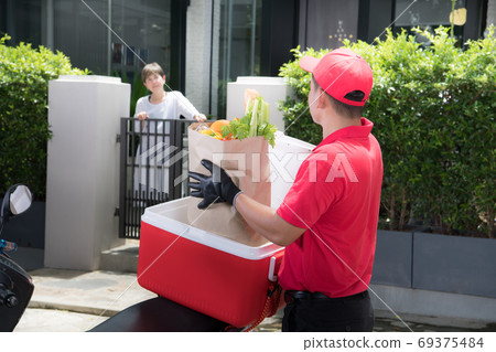 Asian delivery man delivering  groceries bag of food, fruit, vegetable and drink to woman recipient  69375484