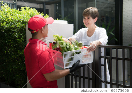 Asian delivery man delivering  groceries bag of food, fruit, vegetable and drink to woman recipient  69375606