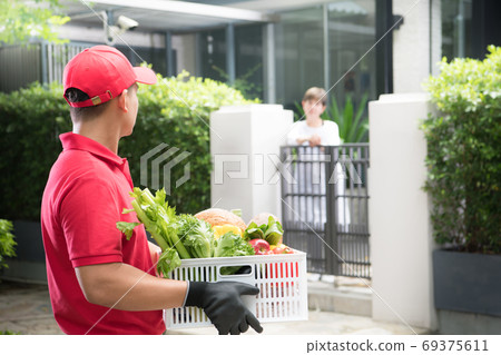 Asian delivery man delivering  groceries bag of food, fruit, vegetable and drink to woman recipient  69375611