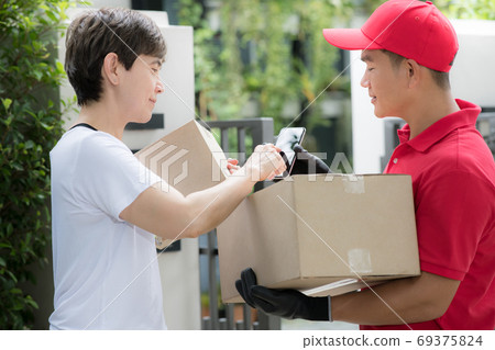 Asian delivery man in red uniform delivering parcel box to woman recipient at home 69375824