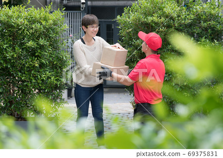 Asian delivery man in red uniform delivering parcel box to woman recipient at home 69375831