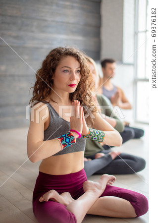 Athletic young people practicing yoga lesson indoors sitting in line against grey wall Athletic young people practicing yoga lesson indoors sitting in line against grey wall 69376182