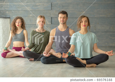 Yoga training indoors. Meditating people sitting on the floor with crossed legs. Yoga training indoors. Meditating people sitting on the floor with crossed legs. 69376188