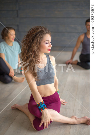 Woman training yoga in cow head pose in gym at grey studio background 69376678