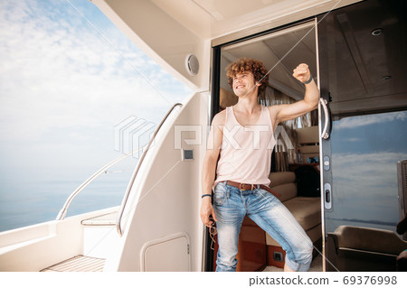 Young handsome man preparing boat to start a journey, standing on the boat Young handsome man preparing boat to start a journey, standing on the boat 69376998
