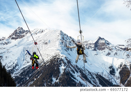 Scenic view couple of tourist with skiing equipment enjoy having fun riding suspended zipline wire  69377172
