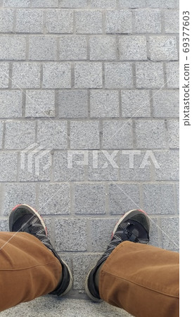 Legs of seated man in shabby trousers and sneakers 69377603