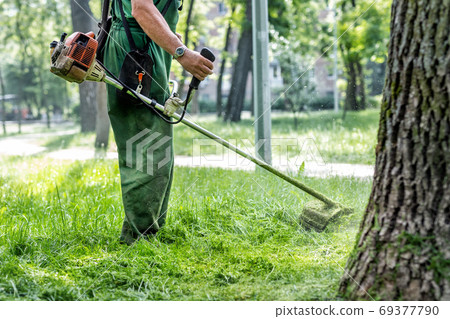 Worker mowing tall grass with electric or petrol Worker mowing tall grass with electric or petrol 69377790