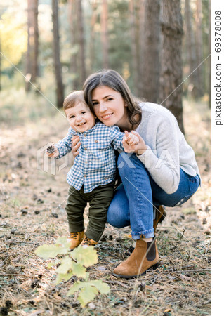 Outdoor autumn portrait of young pretty woman mother posing in autumn pine forest with her lovely cute little son, laughing together. Outdoor autumn portrait of young pretty woman mother posing in autumn pine forest with her lovely cute little son, laughing together. 69378008