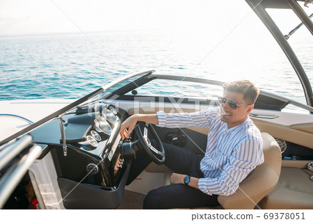 Aspirational successful businessman standing by luxury boats and yachts against a deep blue sky, holding his jacket over his shoulder. 69378051