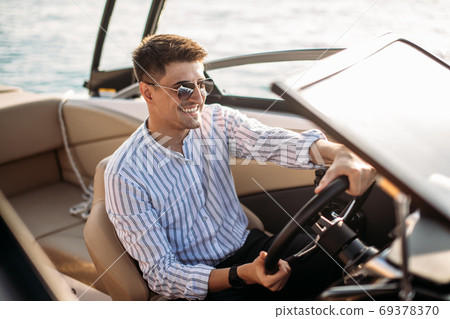 Aspirational successful businessman standing by luxury boats and yachts against a deep blue sky, holding his jacket over his shoulder. 69378370
