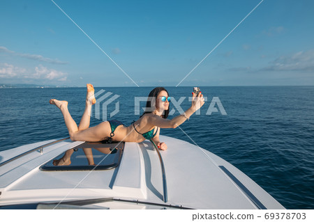 Young woman in swimsuit taking selfie portrait while sunbathing on luxury yacht 69378703