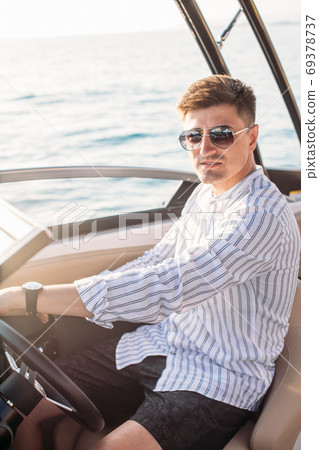 Aspirational successful businessman standing by luxury boats and yachts against a deep blue sky, holding his jacket over his shoulder. 69378737