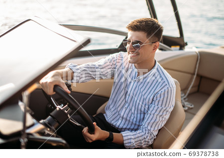 Aspirational successful businessman standing by luxury boats and yachts against a deep blue sky, holding his jacket over his shoulder. 69378738