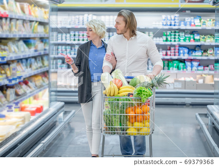 Couple in a supermarket shopping with full food cart buying groceries Couple in a supermarket shopping with full food cart buying groceries 69379368