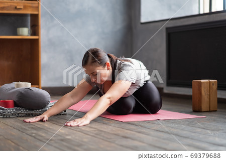 Woman working out indoors, doing variation of twisted forward bend yoga exercise Woman working out indoors, doing variation of twisted forward bend yoga exercise 69379688