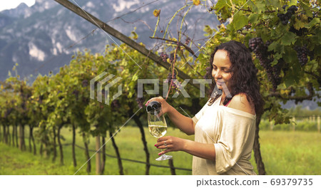 Young woman with a glass of white wine in the vineyards of Italy. Person pouring wine. Free space 69379735