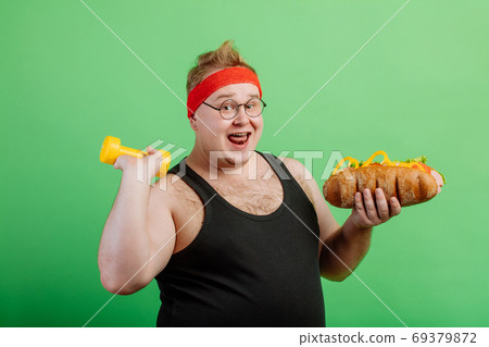 joyful fat male haqving fun with burger and dumbbell joyful fat male haqving fun with burger and dumbbell 69379872