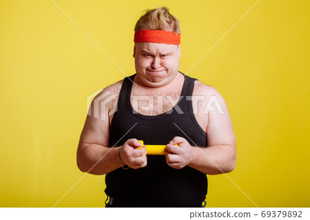 Fat man try to lift small yellow dambbell 69379892