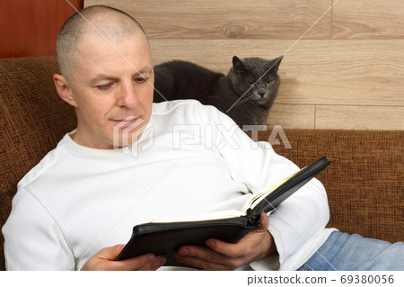 man reading a book relaxing on the couch with the cat man reading a book relaxing on the couch with the cat 69380056