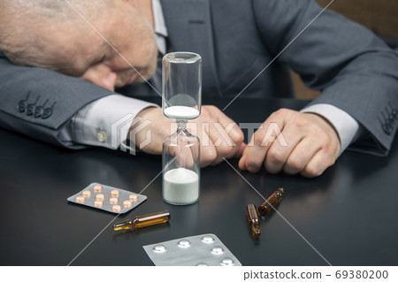 hourglass on the background of a tired and depressed business ma hourglass on the background of a tired and depressed business ma 69380200