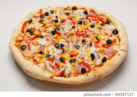 Italian pizza with slices of sausage, tomatoes, sweet pepper and corn, on a wooden board 69387157