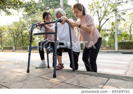 Asian mother and daughter help,care,support outdoor senior grandmother after cross the road,barrier from footpath,sidewalk is tall,different level area,elderly with walker,leg pain,lifestyle problem 69389591