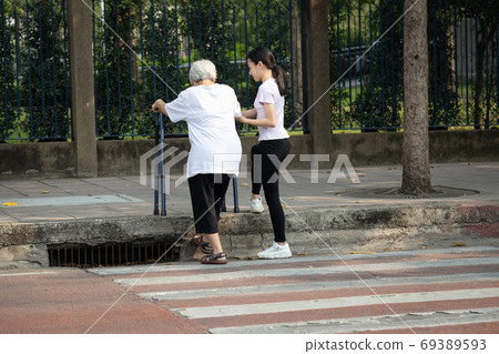 Asian senior woman was trying to walk up the sidewalk with walker after cross the road on crosswalk, the footpath level is higher than the road, different level floor, problems of elderly or disabled Asian senior woman was trying to walk up the sidewalk with walker after cross the road on crosswalk, the footpath level is higher than the road, different level floor, problems of elderly or disabled 69389593